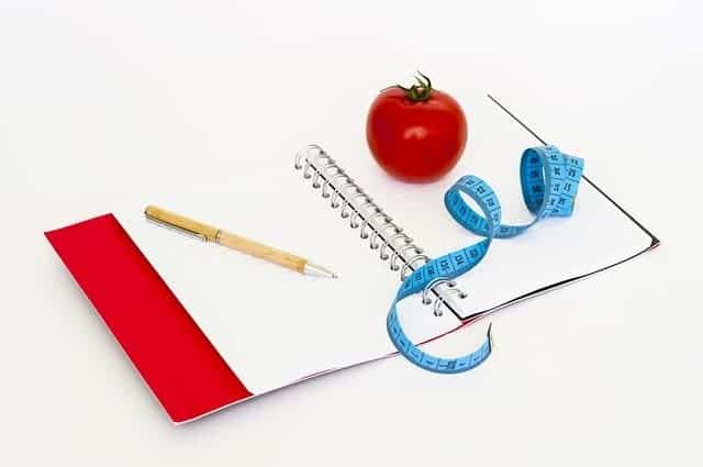 a notebook, a pen, a measuring tape and a tomato