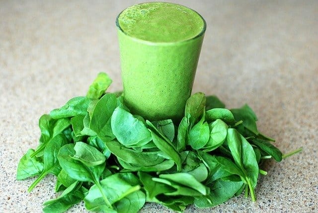 A glass with a green smoothie, spinach leaves all around