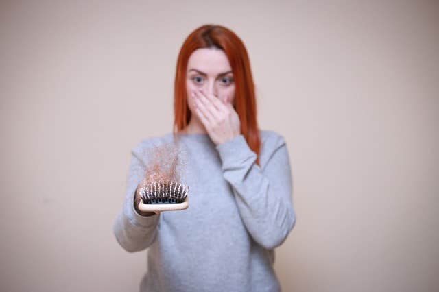 a woman looks at a hairbrush full of hair