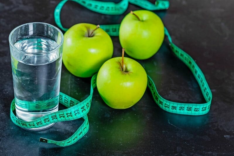 A glass of water, green apples and a measuring tape