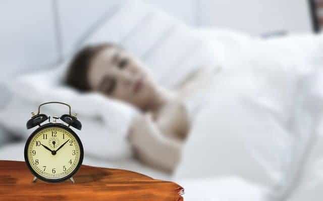 a woman sleeps, there is an alarm clock by the bed