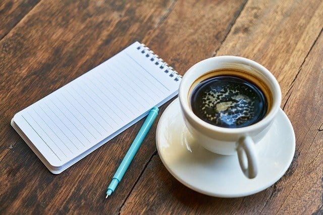 a cup of coffee, a notebook, a pen