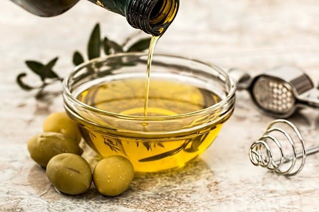 oil poured into a bowl, next to green olives