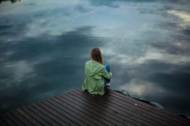 a woman sits on the edge of a pier and looks into the water