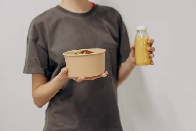 woman holds a bowl of food and a shake
