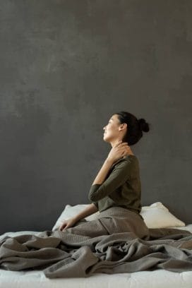 woman sitting on a bed and holding her neck, back pain