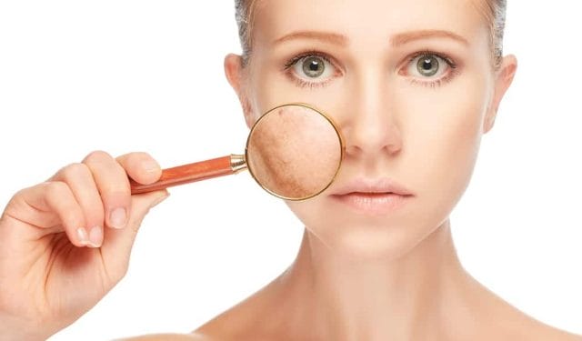 A woman looks at her complexion through a magnifying glass