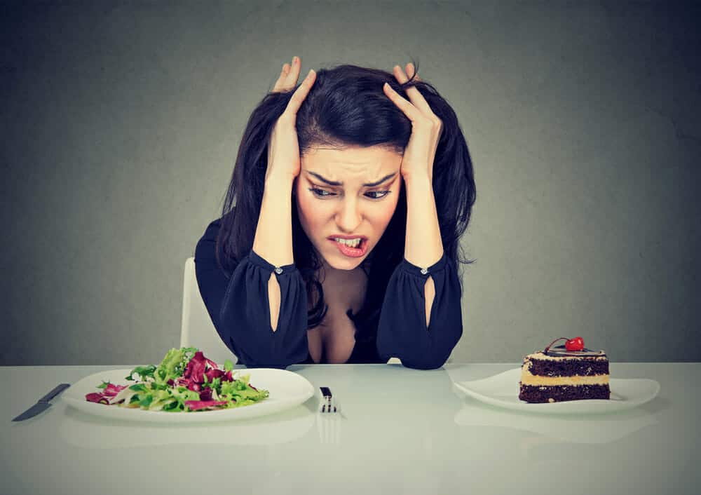 a woman sits at a table with a plate of cake and a plate of salad