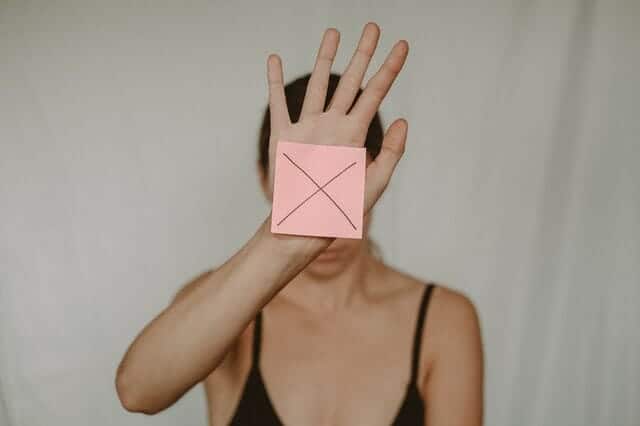a sad woman holds a cardboard box with the x sign in front of her