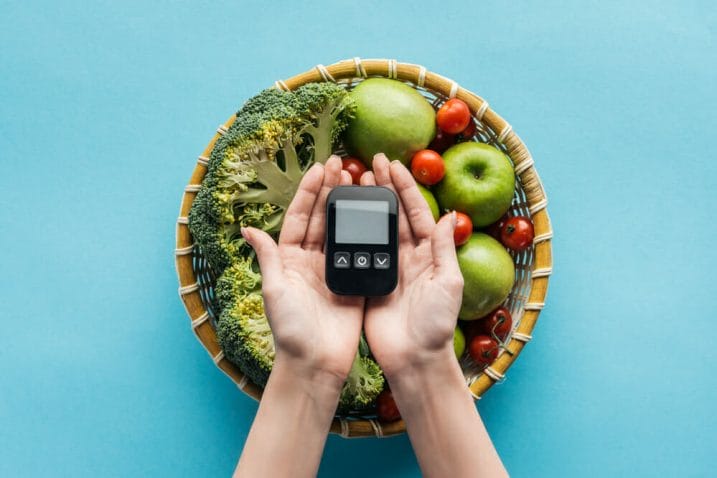  A bowl with vegetables and fruit, next to a glucose meter held in the hands