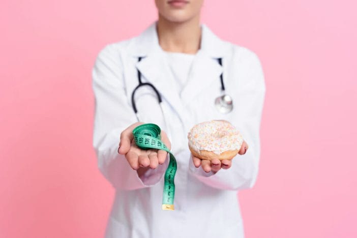 doctor holds a donut with icing in one hand and a centimeter in the other