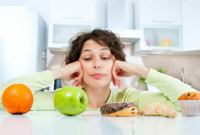 a woman wonders whether to eat fruit or biscuits