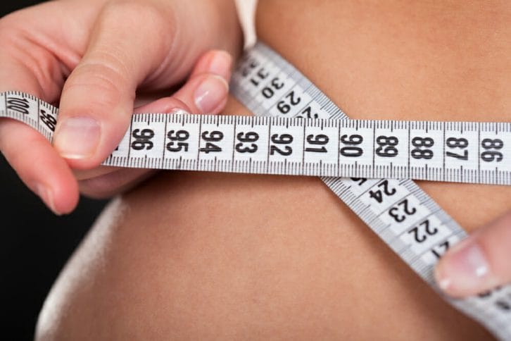 a woman measures her waist with a centimeter
