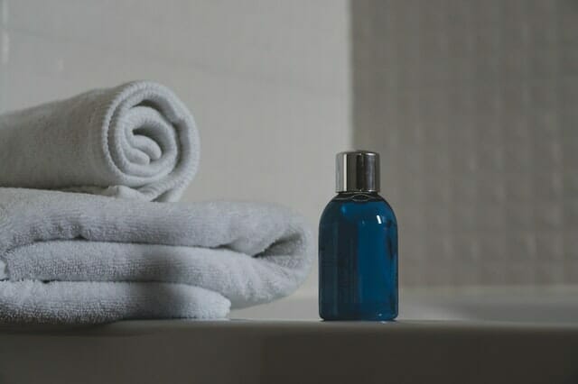  blue bottle with shampoo, towels next to it