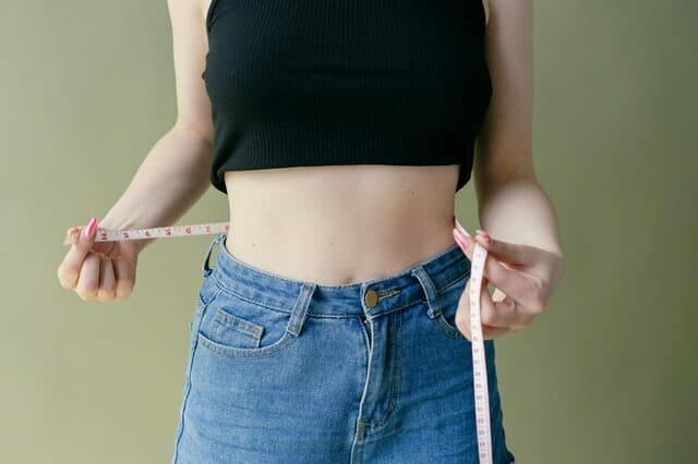 a woman measures her waist with a centimetre
