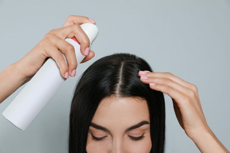 woman applies dry shampoo on her hair
