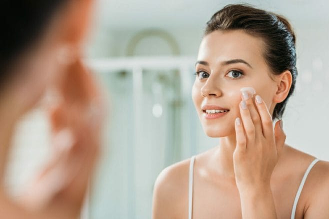 a woman pats the cream into her cheeks