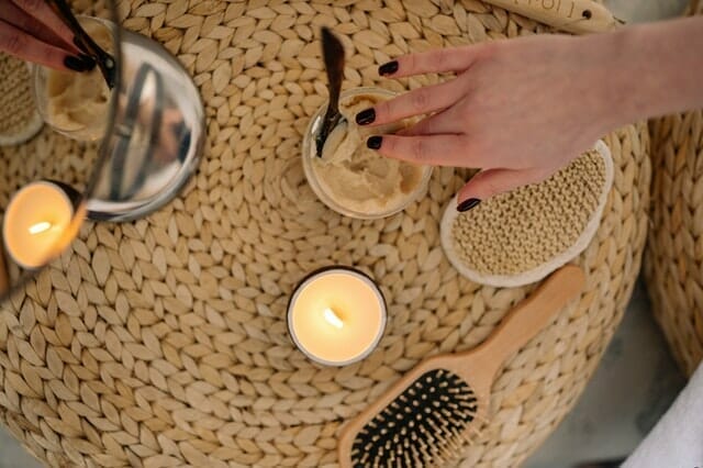 a woman reaches her hand into a jar of cream