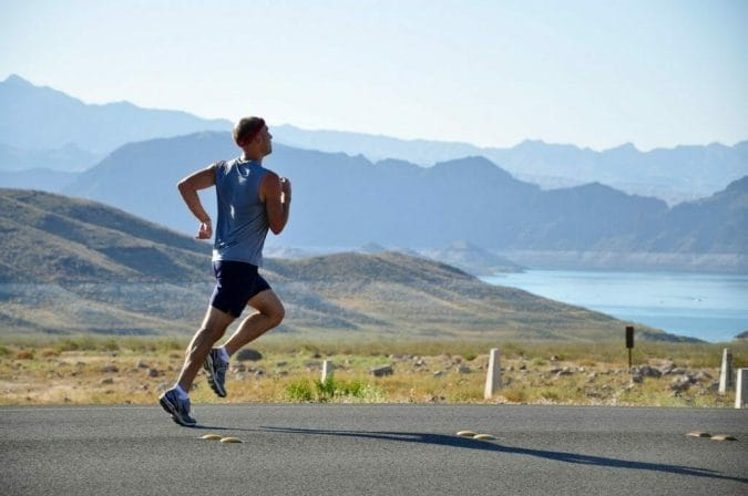 A man jogs, with mountains and a lake in the background