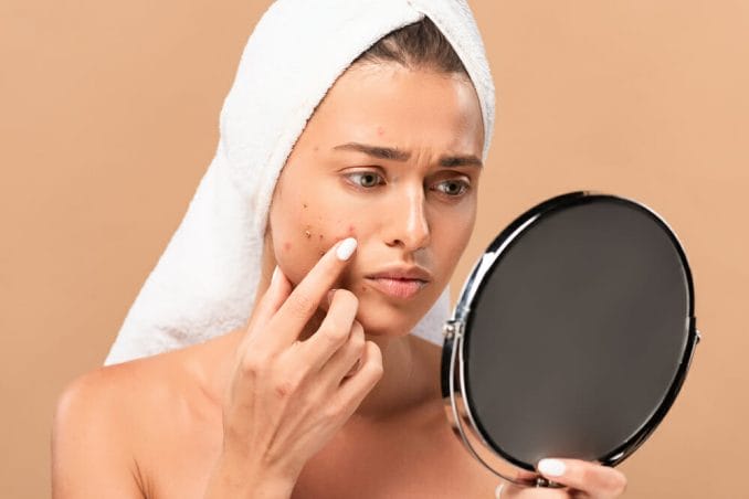 A woman watches the pimples on her face in the mirror