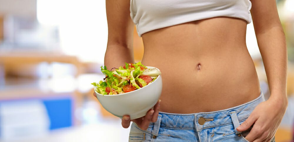 A slim woman holds a salad bowl of vegetables