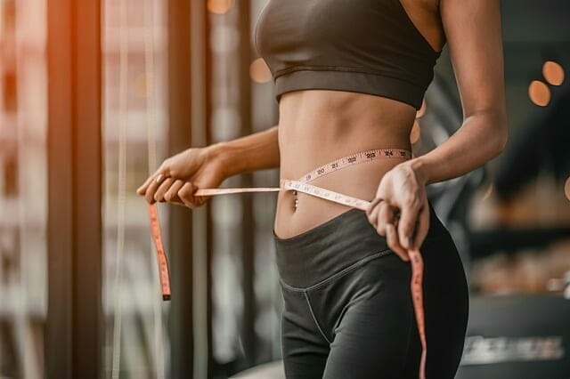 A woman measures her waist with a centimeter