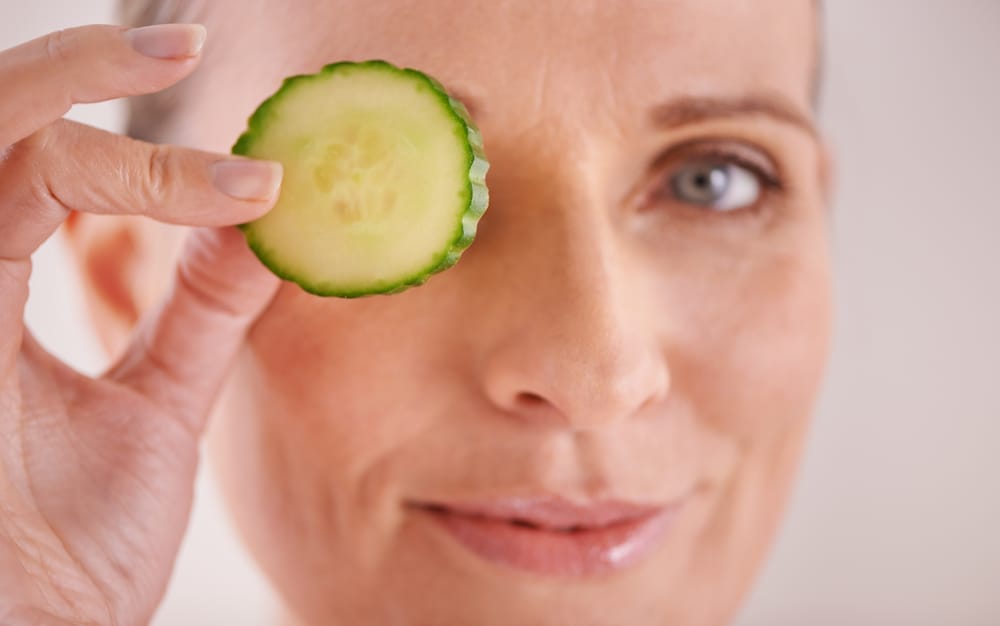  A woman holds a cucumber slice to her eye