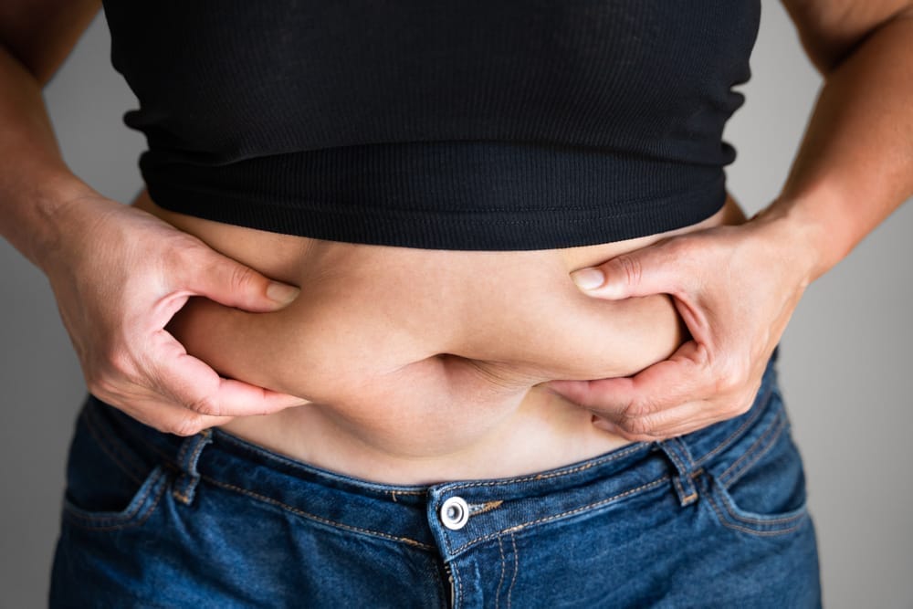 A woman holds her belly and observes fat gain